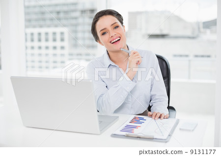Happy businesswoman with graphs and laptop in office Happy businesswoman with graphs and laptop in office 9131177