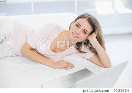Gleeful young woman posing lying on her bed smiling at camera 9131364