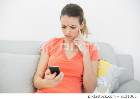 Troubled brunette woman using her smartphone sitting on couch 9131365