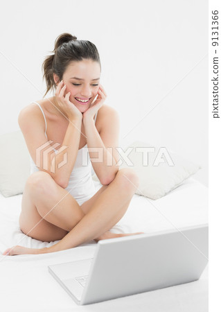 Smiling casual woman with laptop sitting on bed Smiling casual woman with laptop sitting on bed 9131366