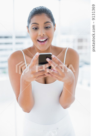 Excited toned brunette holding mobile phone Excited toned brunette holding mobile phone 9131369