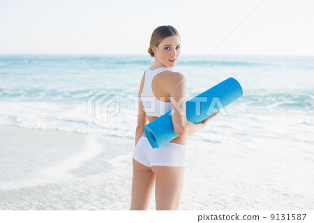 Happy slender woman holding rolled up exercise mat Happy slender woman holding rolled up exercise mat 9131587
