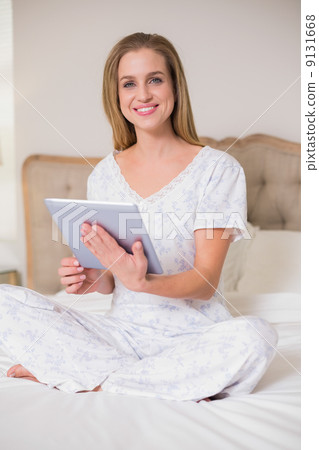 Natural cheerful woman sitting on bed using tablet Natural cheerful woman sitting on bed using tablet 9131668