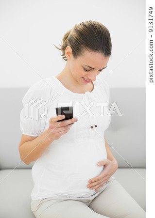 Beautiful pregnant woman holding her smartphone holding happily Beautiful pregnant woman holding her smartphone holding happily 9131749