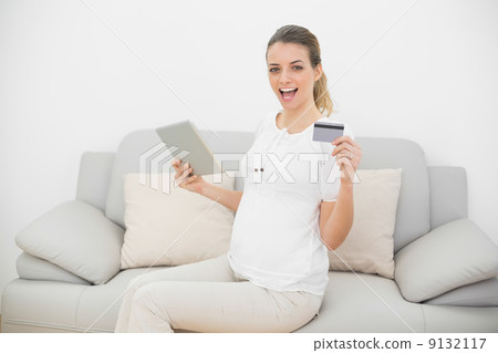 Cheering pregnant woman showing her tablet and credit card looki 9132117