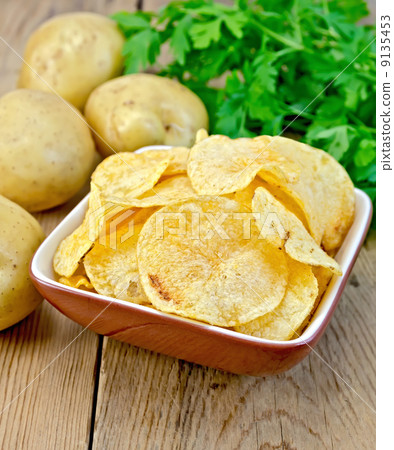 Chips in a bowl with a potato on the board Chips in a bowl with a potato on the board 9135453