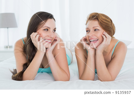 Cheerful female friends in teal tank tops lying in bed 9135937