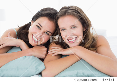 Two smiling young female friends lying in bed 9136151