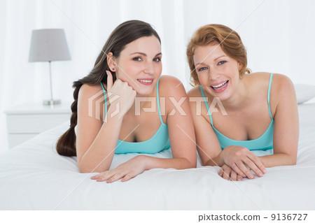 Happy female friends in teal tank tops lying in bed 9136727