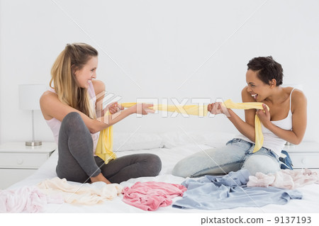 Female friends jokingly fighting over clothes on bed 9137193