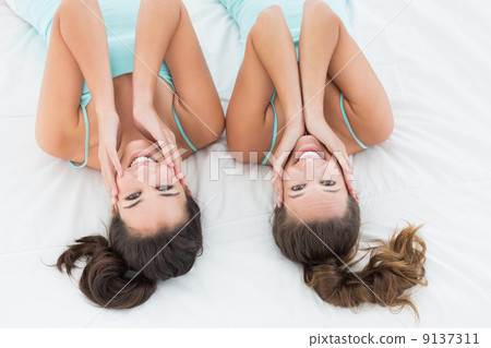 Two female friends in teal tank tops lying in bed 9137311