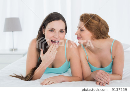 Female friends in tank tops gossiping in bed Female friends in tank tops gossiping in bed 9137339