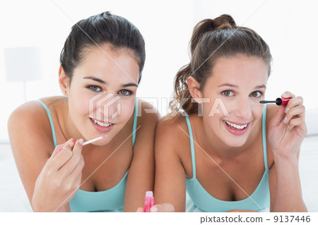 Two young female friends applying make-up in bed Two young female friends applying make-up in bed 9137446