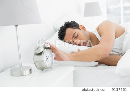 Sleepy man extending hand to alarm clock 9137561