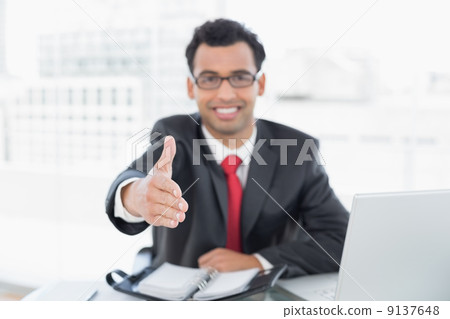 Blurred businessman offering a handshake at office desk 9137648