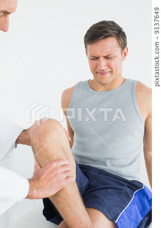 Displeased young man getting his leg examined Displeased young man getting his leg examined 9137649