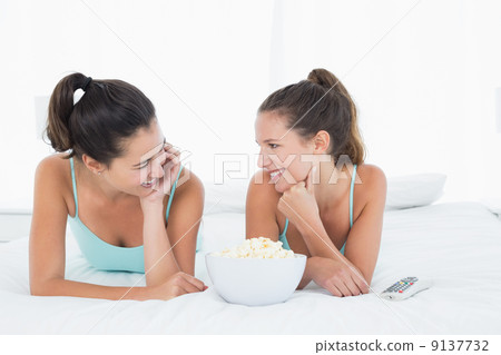 Smiling female friends with popcorn bowl lying in bed 9137732