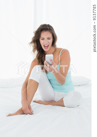 Woman shouting into mobile phone in bed 9137785