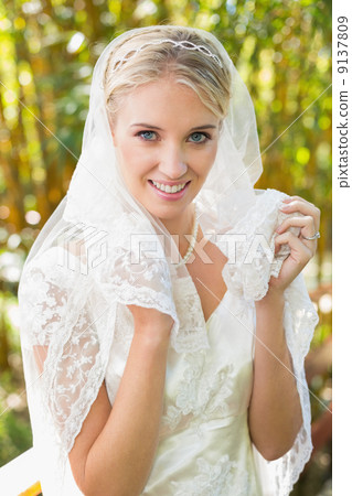 Beautiful blonde bride holding her veil looking at camera happil Beautiful blonde bride holding her veil looking at camera happil 9137809