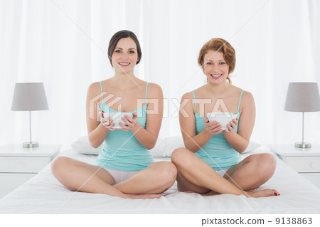 Smiling female friends with salad bowls sitting on bed 9138863