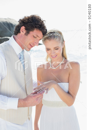 Handsome man placing ring on smiling blonde brides finger 9140180