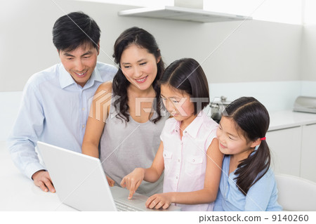 Family of four using laptop in kitchen 9140260