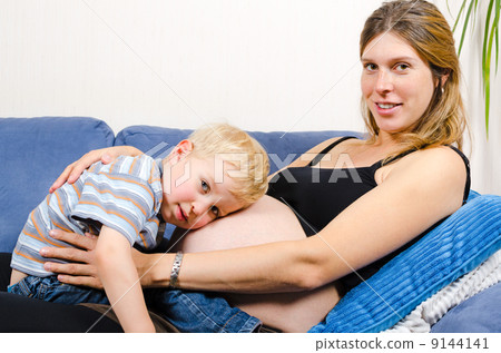 Smiling pregnant mother with her little boy on sofa 9144141