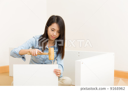 Asian woman using hammer for assembling cupboard Asian woman using hammer for assembling cupboard 9168962