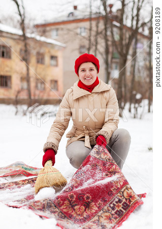 girl in red cap cleans carpet with snow in winter day 9208189