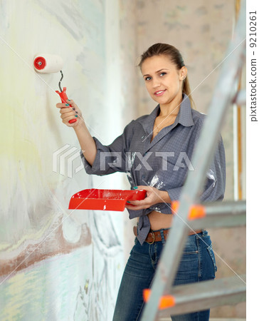 woman paints wall with roller at home woman paints wall with roller at home 9210261