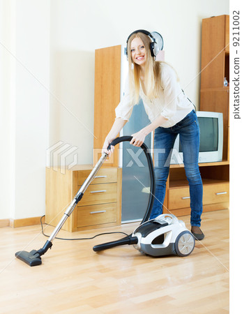 Stock Photo: cheerful blonde woman in headphones with vacuum cleaner