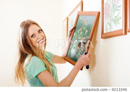 Happy blonde woman hanging picture with flowers Happy blonde woman hanging picture with flowers 9211046