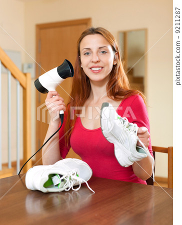 Girl dries the running shoes with hair dryer Girl dries the running shoes with hair dryer 9211287