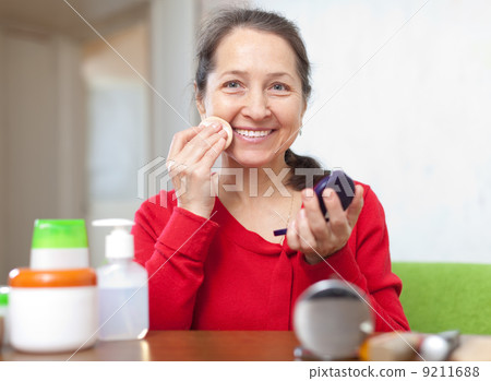 Happy mature woman puts facepowder 9211688