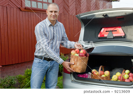 Guy puts apples in the trunk of car 9213609