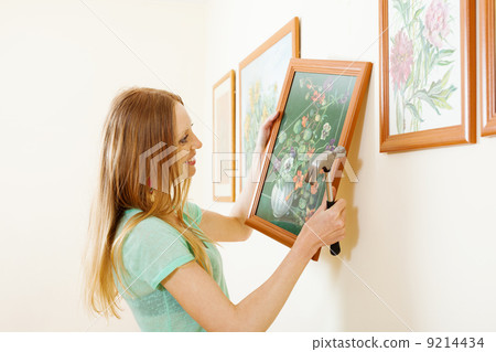 Smiling blonde woman hanging picture Smiling blonde woman hanging picture 9214434