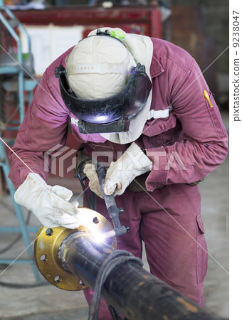 Craftsman in a safety suit is welding a metal pipe 9238047