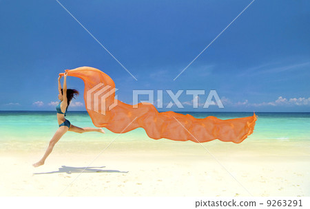 Beautiful young woman jumping on the beach with a colored tissue 9263291