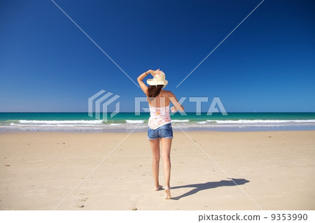 walking holding on straw hat at beach 9353990