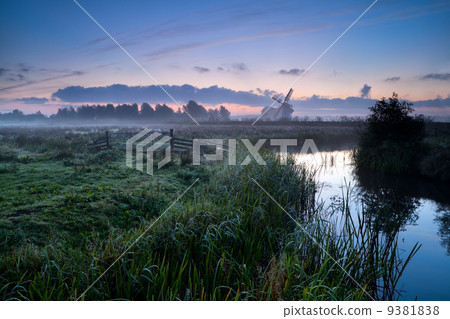 misty morning over Dutch farmland with windmill and river 9381838