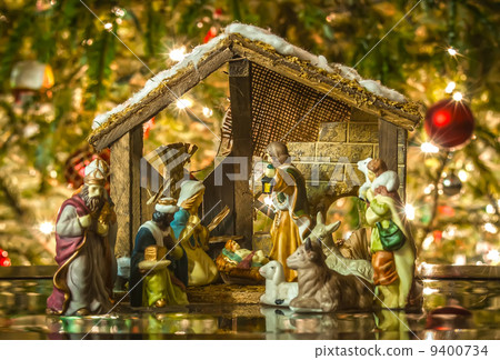 Old handmade nativity scene in front of a christmas tree 9400734