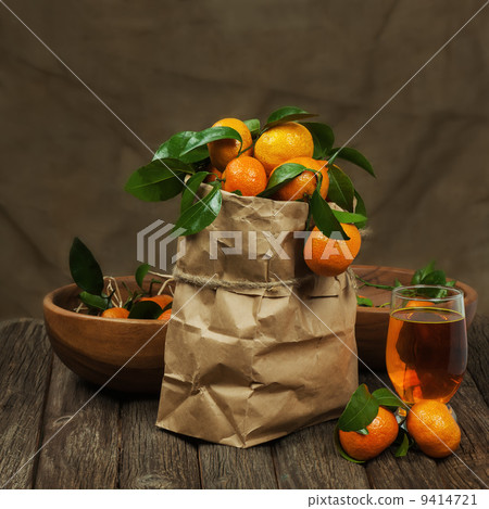 Fresh tangerines in recycle paper bag and glass of juice on wood 9414721