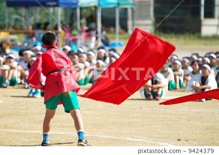 一個男孩在小學運動會的支持戰鬥中搖晃紅旗 9424379