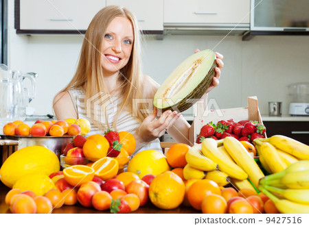 Happy blonde woman near heap of fruits at home kitchen 9427516