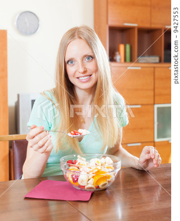 Positive woman eating fruit salad at home Positive woman eating fruit salad at home 9427553