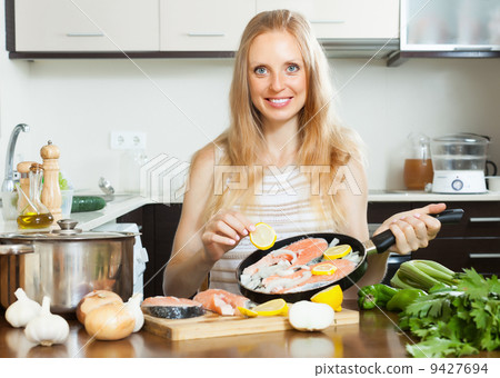 Smiling woman cooking salmon with lemon 9427694