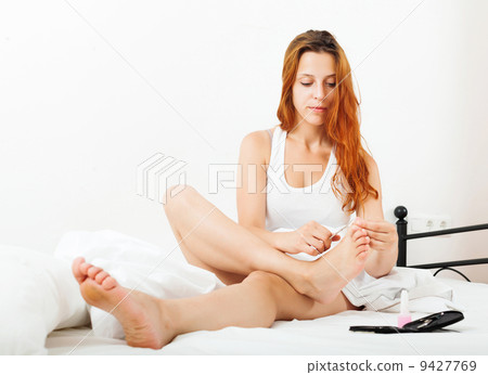 Red-haired girl cares for toenails 9427769