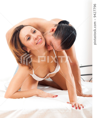 Happy adult couple having sex on bed in bedroom..