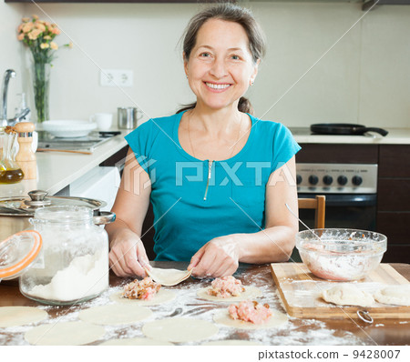 Smiling mature woman making meat dumplings Smiling mature woman making meat dumplings 9428007