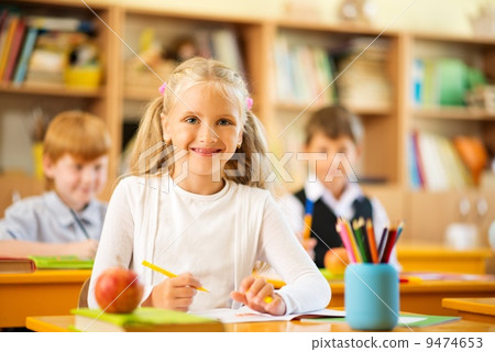Little schoolgirl sitting behind school desk during lesson in school 9474653
